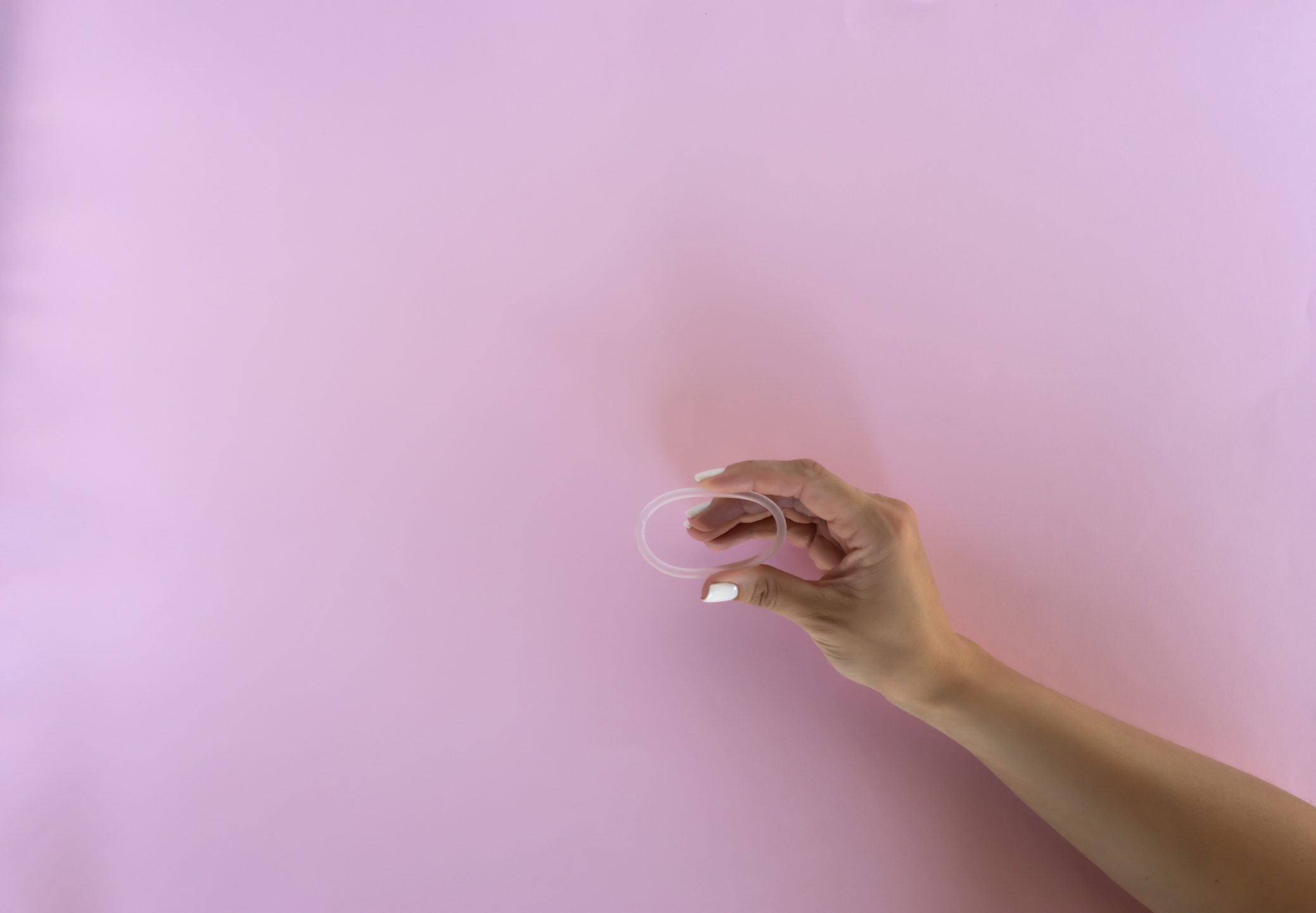 Hand holding a contraceptive ring, pink background.