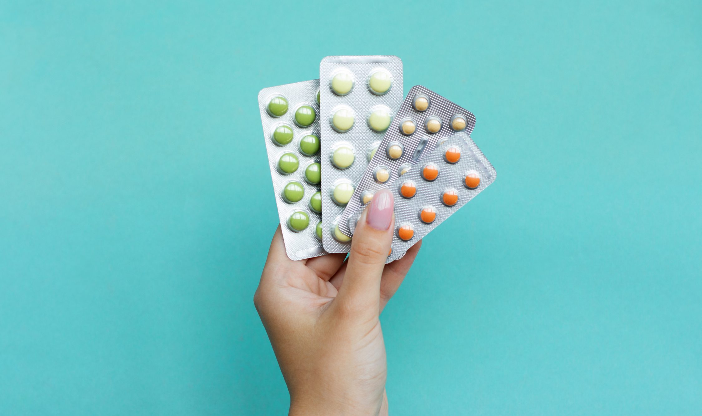 A hand holding three packages of pills.